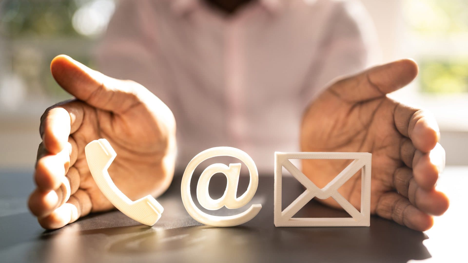 Manos protegiendo símbolos de teléfono, correo y contacto